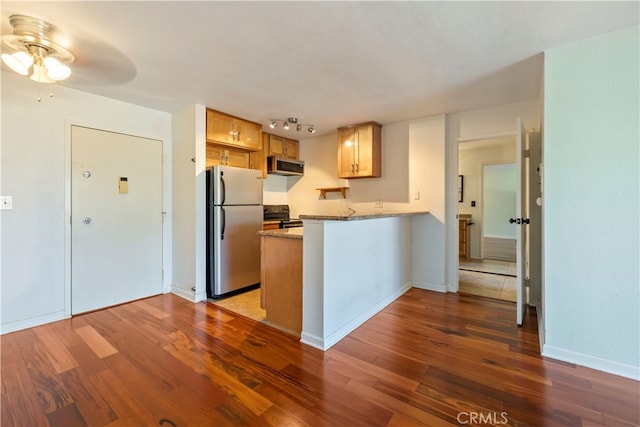 kitchen featuring kitchen peninsula, ceiling fan, stainless steel appliances, dark hardwood / wood-style floors, and light stone counters