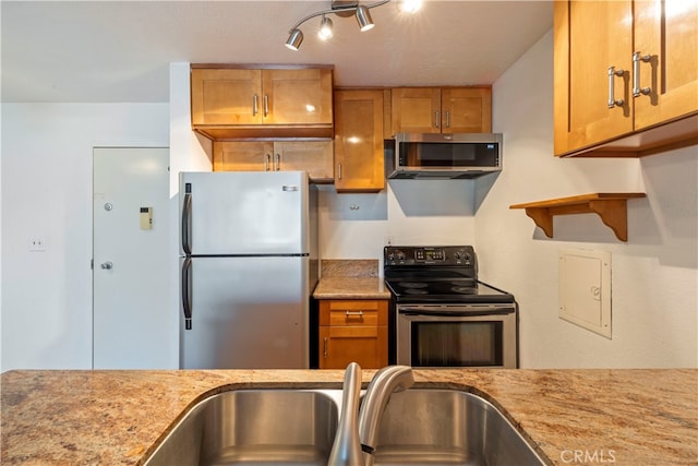 kitchen with stainless steel appliances, rail lighting, light stone counters, and sink