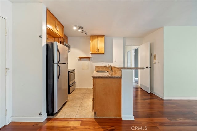 kitchen with light hardwood / wood-style floors, kitchen peninsula, stainless steel appliances, light stone countertops, and sink