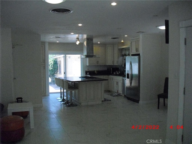 kitchen featuring stainless steel fridge, wall chimney range hood, light tile patterned floors, a kitchen island, and black cooktop