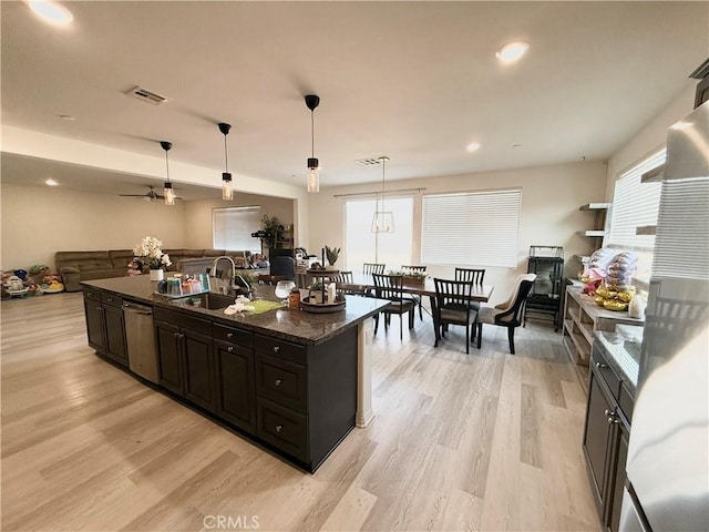 kitchen with sink, a center island with sink, decorative light fixtures, stainless steel dishwasher, and dark stone counters