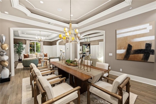 dining room featuring a chandelier, wood-type flooring, a tray ceiling, and ornamental molding