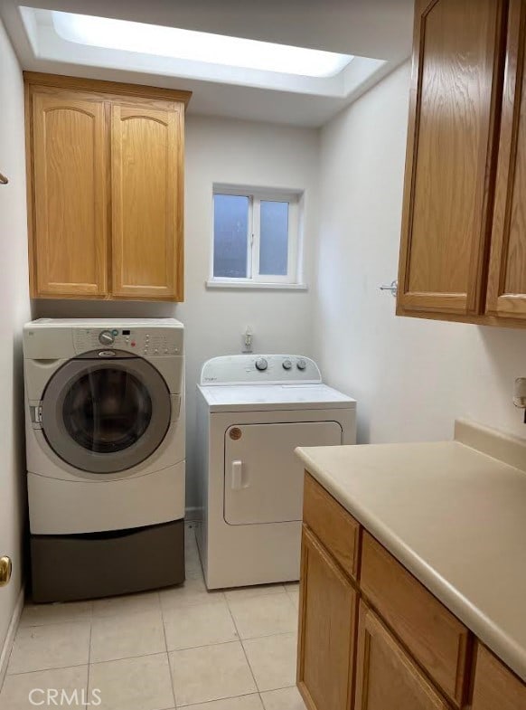 clothes washing area featuring light tile patterned floors, cabinets, and washer and clothes dryer