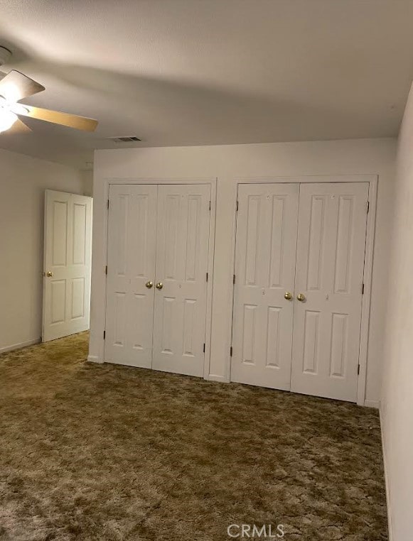 unfurnished bedroom featuring ceiling fan, carpet floors, and multiple closets