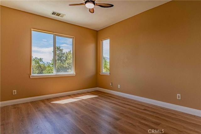 unfurnished room with a ceiling fan, visible vents, baseboards, and wood finished floors