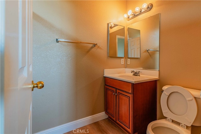 half bath with wood finished floors, vanity, toilet, and baseboards