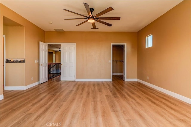 unfurnished bedroom with light wood finished floors, a spacious closet, and baseboards