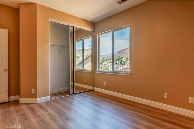 unfurnished bedroom with a closet, wood finished floors, a mountain view, and baseboards