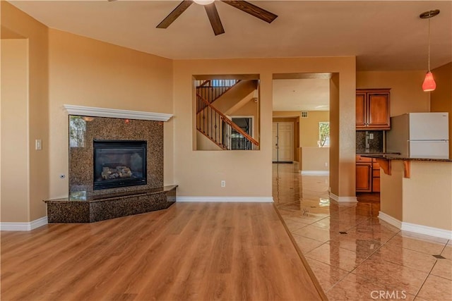 unfurnished living room with light wood finished floors, baseboards, a ceiling fan, stairs, and a high end fireplace