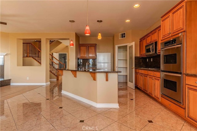 kitchen featuring visible vents, brown cabinetry, appliances with stainless steel finishes, a kitchen breakfast bar, and backsplash