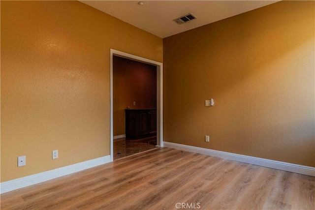 unfurnished room featuring light wood-type flooring, visible vents, and baseboards