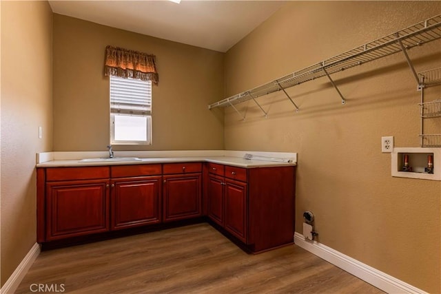 washroom featuring hookup for a washing machine, wood finished floors, a sink, baseboards, and cabinet space