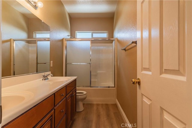 bathroom with toilet, wood finished floors, a sink, combined bath / shower with glass door, and double vanity