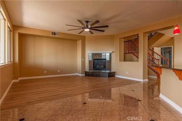 unfurnished living room featuring visible vents, stairway, a premium fireplace, wood finished floors, and baseboards