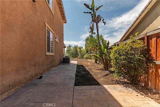 view of side of property featuring stucco siding, a fenced backyard, cooling unit, and a patio