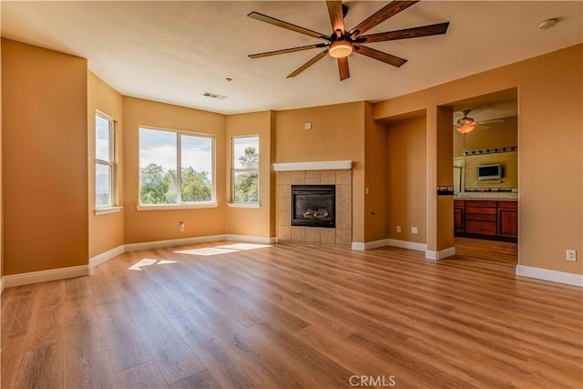 unfurnished living room with visible vents, a tiled fireplace, light wood-style floors, ceiling fan, and baseboards