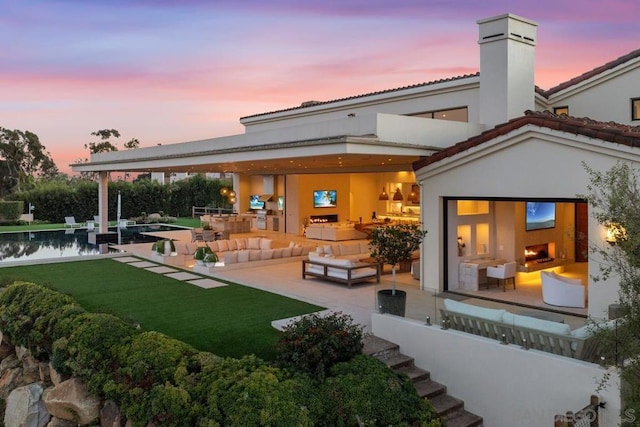 back house at dusk featuring an outdoor hangout area, a patio area, a pool, and exterior kitchen