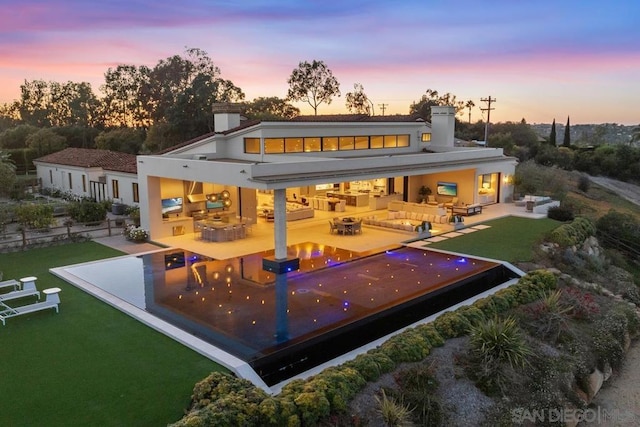 back house at dusk featuring a yard, a patio area, outdoor lounge area, and an outdoor kitchen