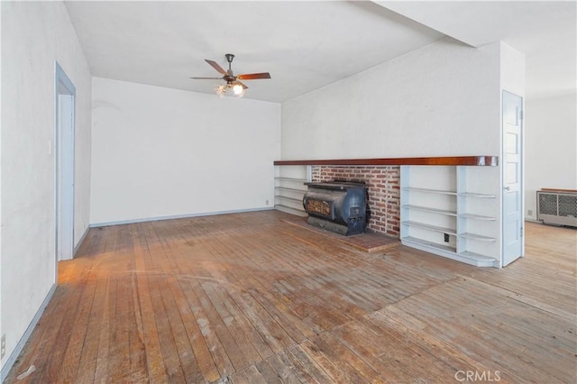 unfurnished living room featuring a wood stove, radiator heating unit, ceiling fan, and light hardwood / wood-style flooring