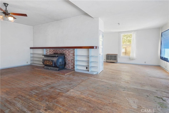 unfurnished living room with ceiling fan, a wood stove, and light hardwood / wood-style floors