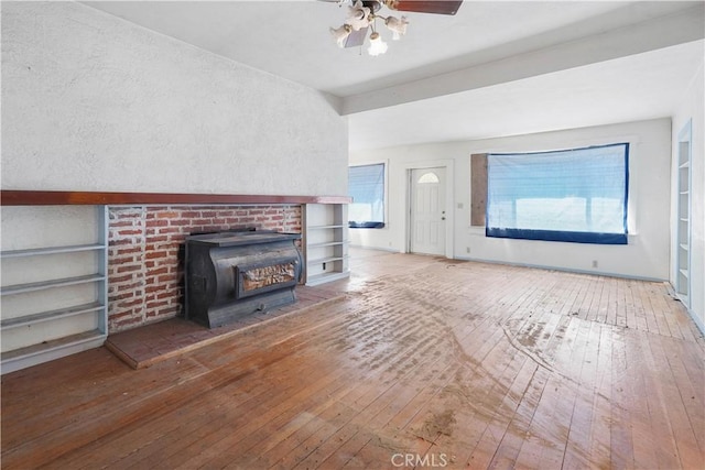 unfurnished living room with hardwood / wood-style flooring, a wood stove, ceiling fan, and built in shelves