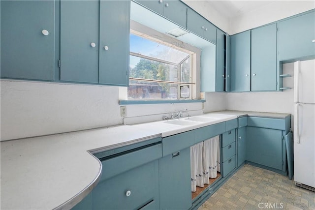 kitchen featuring blue cabinets, sink, and white fridge