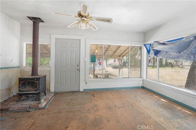 unfurnished sunroom featuring ceiling fan and a wood stove