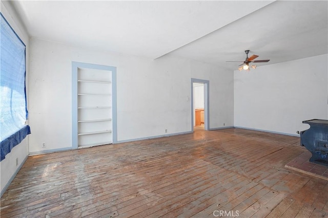 unfurnished living room with ceiling fan, hardwood / wood-style floors, built in features, and a wood stove