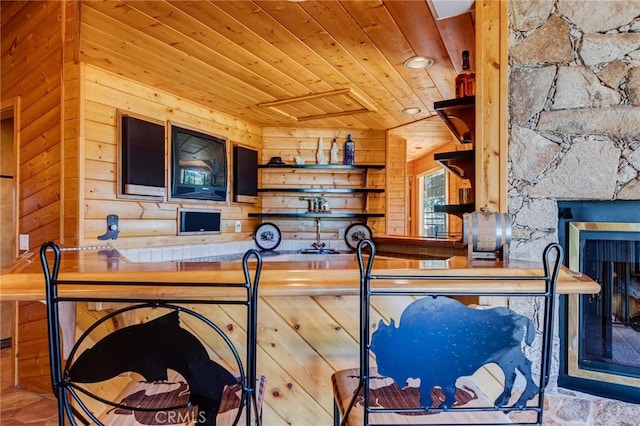 kitchen with a stone fireplace, wood walls, and wooden ceiling