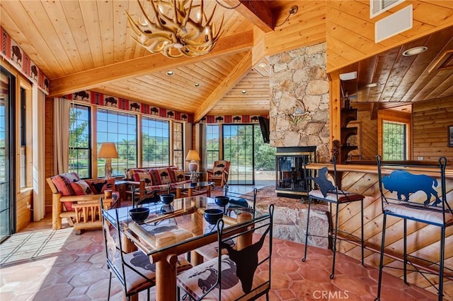 dining room with vaulted ceiling with beams, a stone fireplace, wooden ceiling, and a notable chandelier