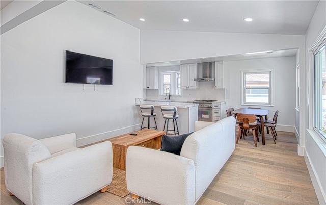 living room with light wood-type flooring, vaulted ceiling, and sink