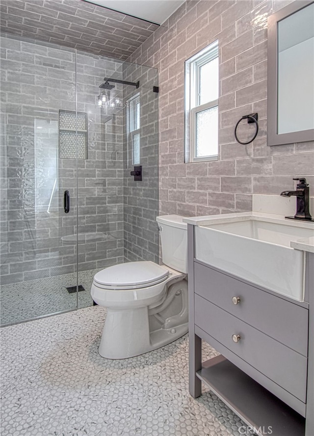 bathroom with an enclosed shower, vanity, toilet, and tile walls