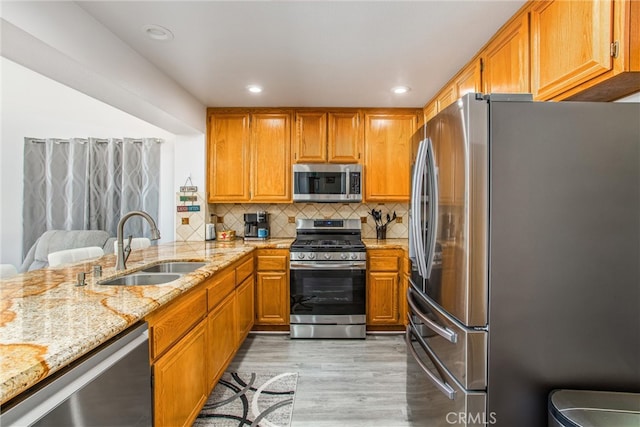 kitchen with stainless steel appliances, sink, light hardwood / wood-style floors, decorative backsplash, and light stone countertops