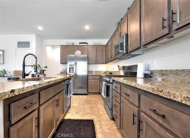 kitchen featuring light stone countertops, appliances with stainless steel finishes, dark brown cabinets, and sink