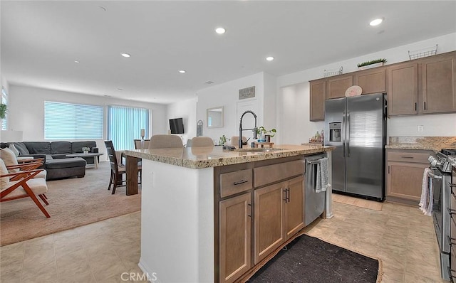 kitchen featuring light stone counters, stainless steel appliances, light colored carpet, sink, and a center island with sink