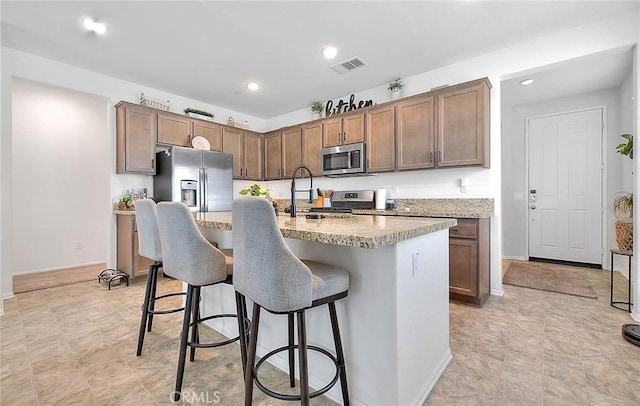 kitchen with a breakfast bar area, light stone countertops, an island with sink, and appliances with stainless steel finishes