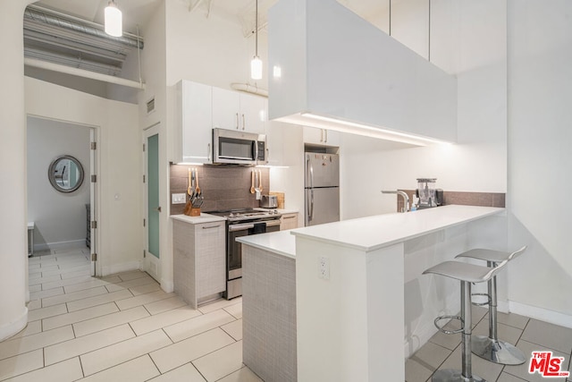 kitchen featuring white cabinetry, tasteful backsplash, stainless steel appliances, a towering ceiling, and decorative light fixtures