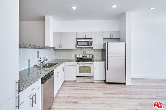 kitchen with stainless steel appliances, gray cabinetry, sink, decorative backsplash, and light wood-type flooring