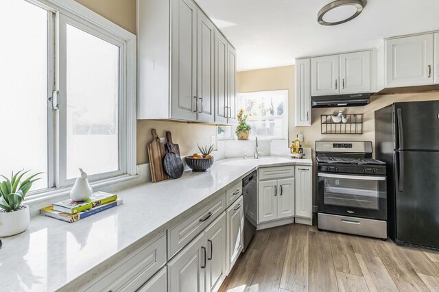 kitchen with white cabinetry, stainless steel appliances, sink, light stone countertops, and light hardwood / wood-style flooring