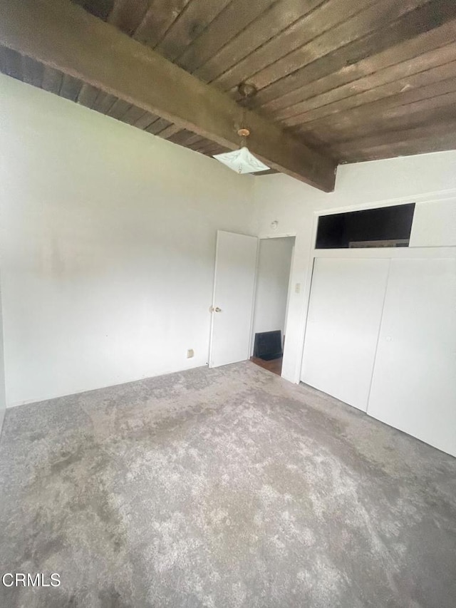 unfurnished bedroom featuring carpet flooring, lofted ceiling with beams, a closet, and wooden ceiling