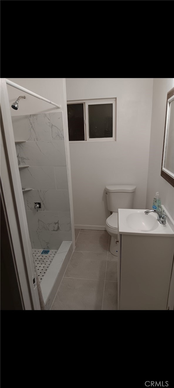 bathroom featuring vanity, a tile shower, toilet, and tile patterned floors