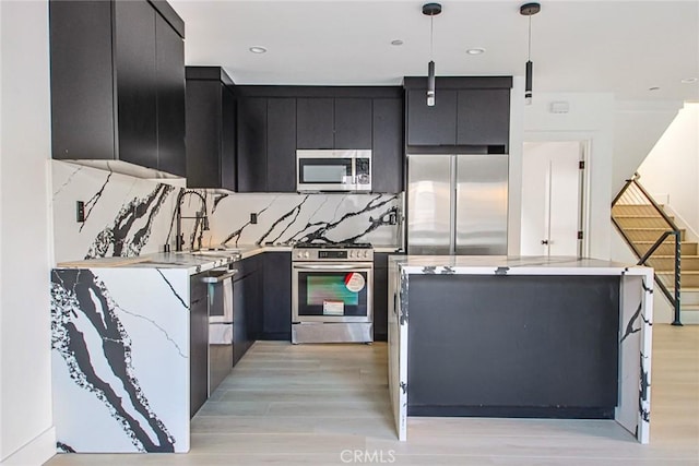 kitchen featuring sink, backsplash, stainless steel appliances, decorative light fixtures, and light wood-type flooring