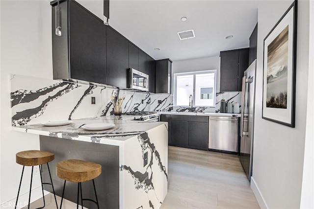 kitchen with sink, stainless steel appliances, tasteful backsplash, a kitchen bar, and kitchen peninsula