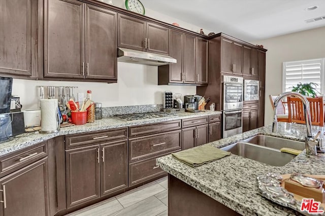 kitchen with light stone countertops, sink, dark brown cabinets, and appliances with stainless steel finishes