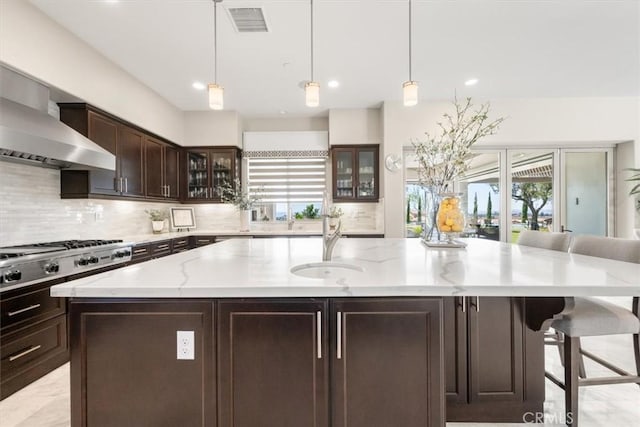 kitchen with decorative light fixtures, a kitchen island with sink, a healthy amount of sunlight, and wall chimney range hood