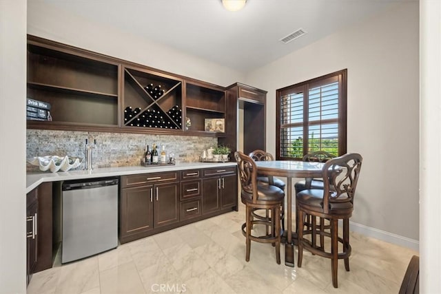 bar with decorative backsplash, dark brown cabinets, and stainless steel dishwasher