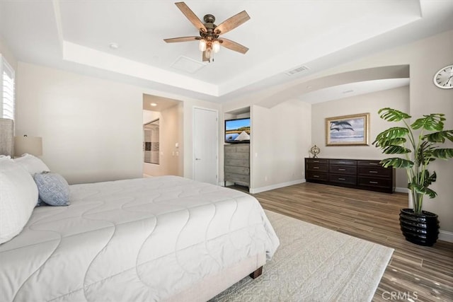 bedroom with dark hardwood / wood-style floors, ceiling fan, and a raised ceiling