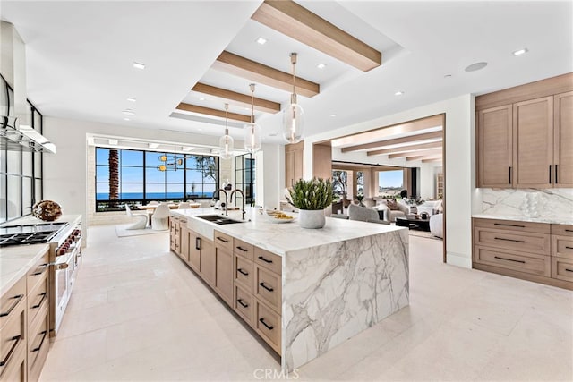 kitchen featuring a spacious island, open floor plan, beamed ceiling, range with gas stovetop, and a sink