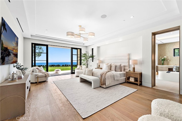 bedroom with light hardwood / wood-style floors, a water view, a chandelier, and a tray ceiling