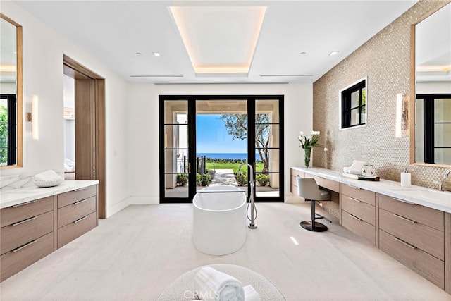 full bath with vanity, decorative backsplash, baseboards, a soaking tub, and an accent wall